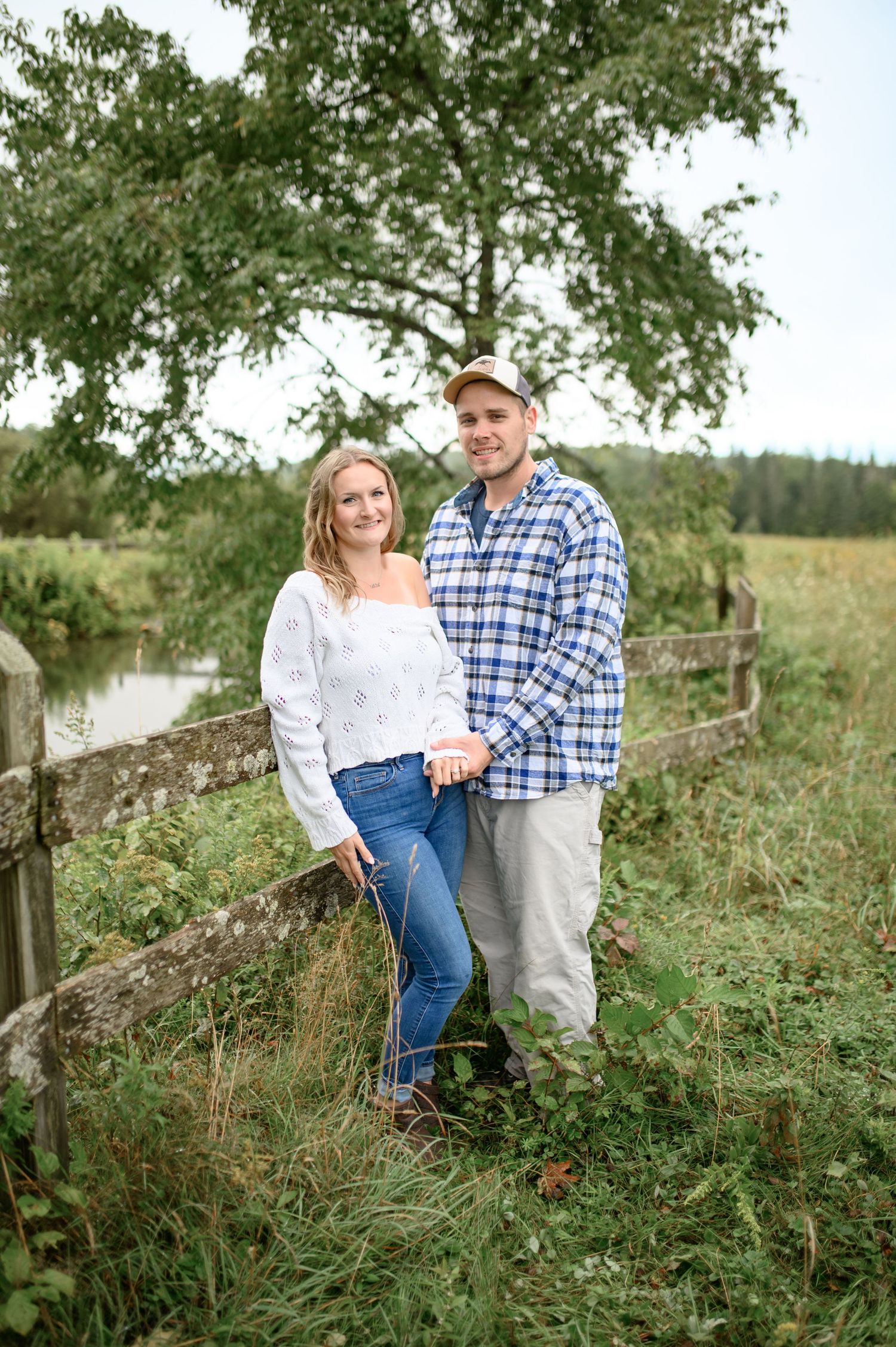 A couple shares a tender moment together in a rustic outdoor setting with tall grass and trees in the background.