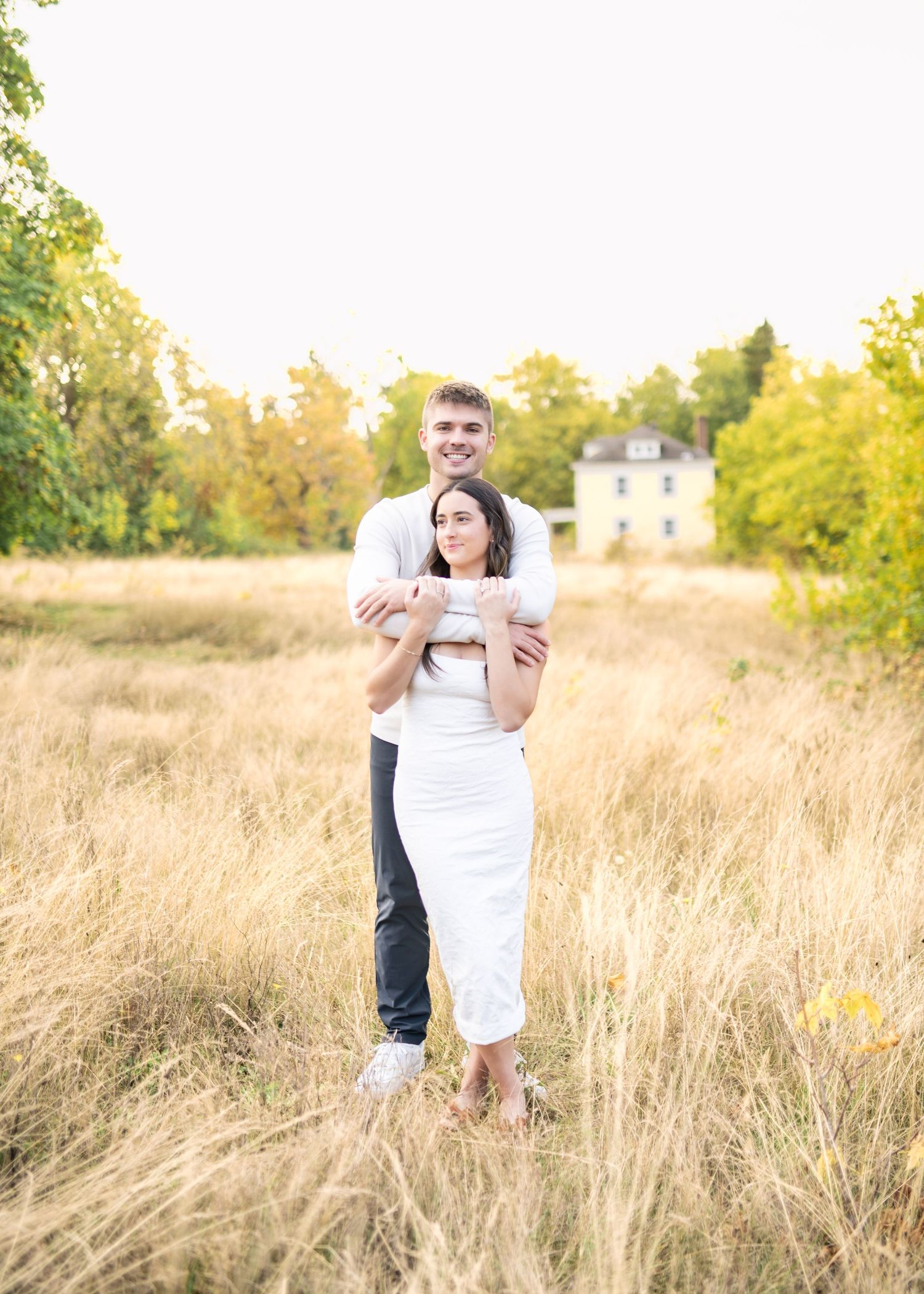 A romantic couple embraces in a golden field of tall grass during a sunny autumn afternoon.