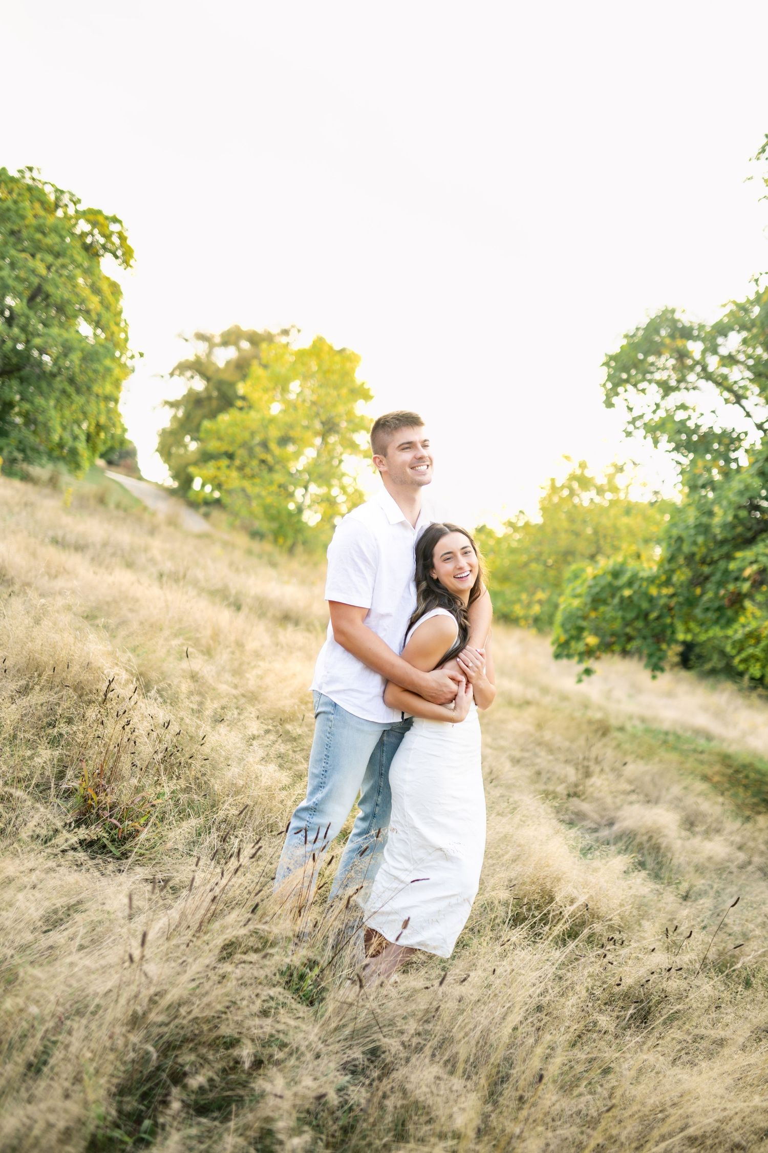 A couple shares a tender moment on a grassy hillside during a sunny summer afternoon.