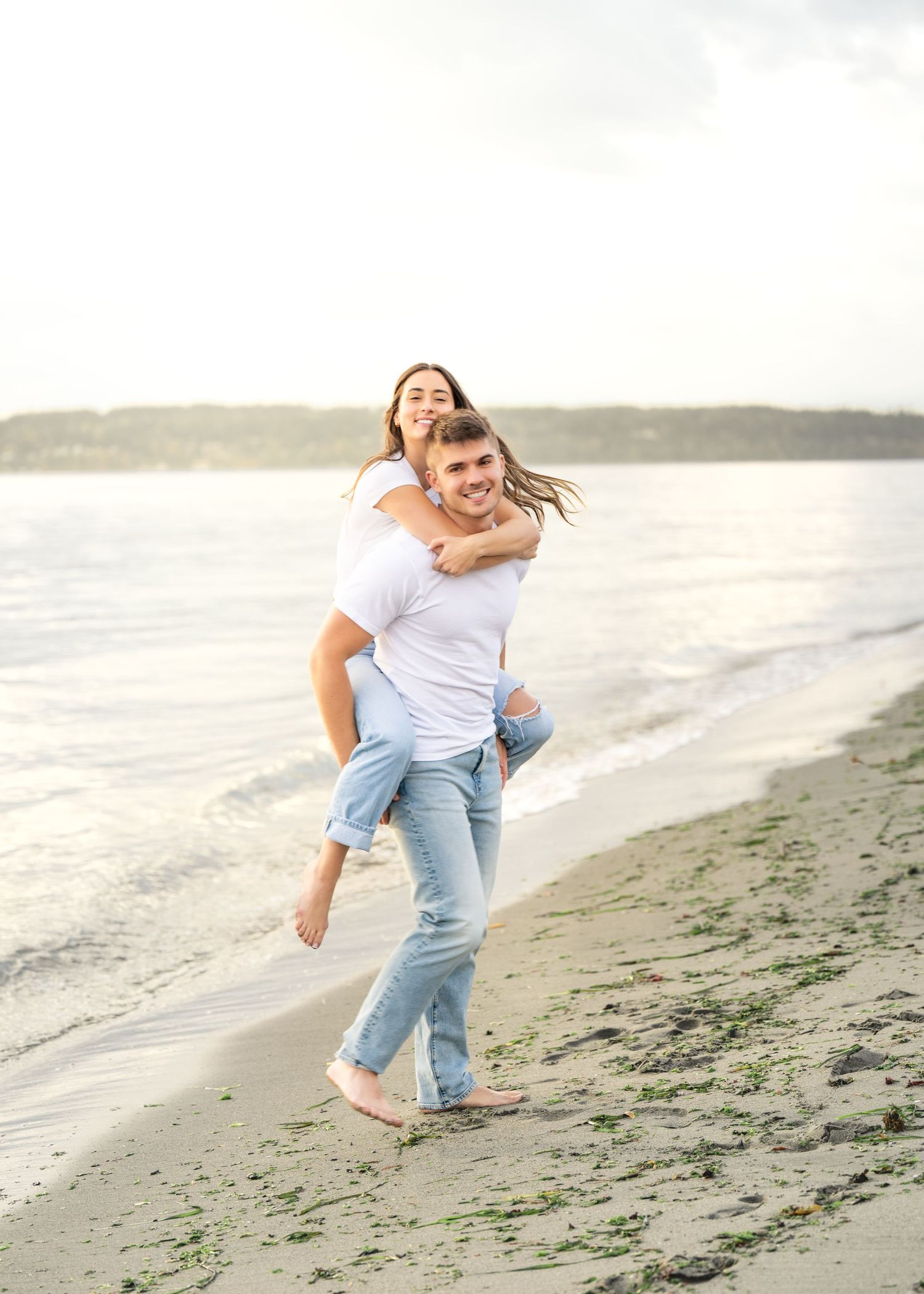 A couple playfully embraces and spins around on a misty beach with waves in the background.