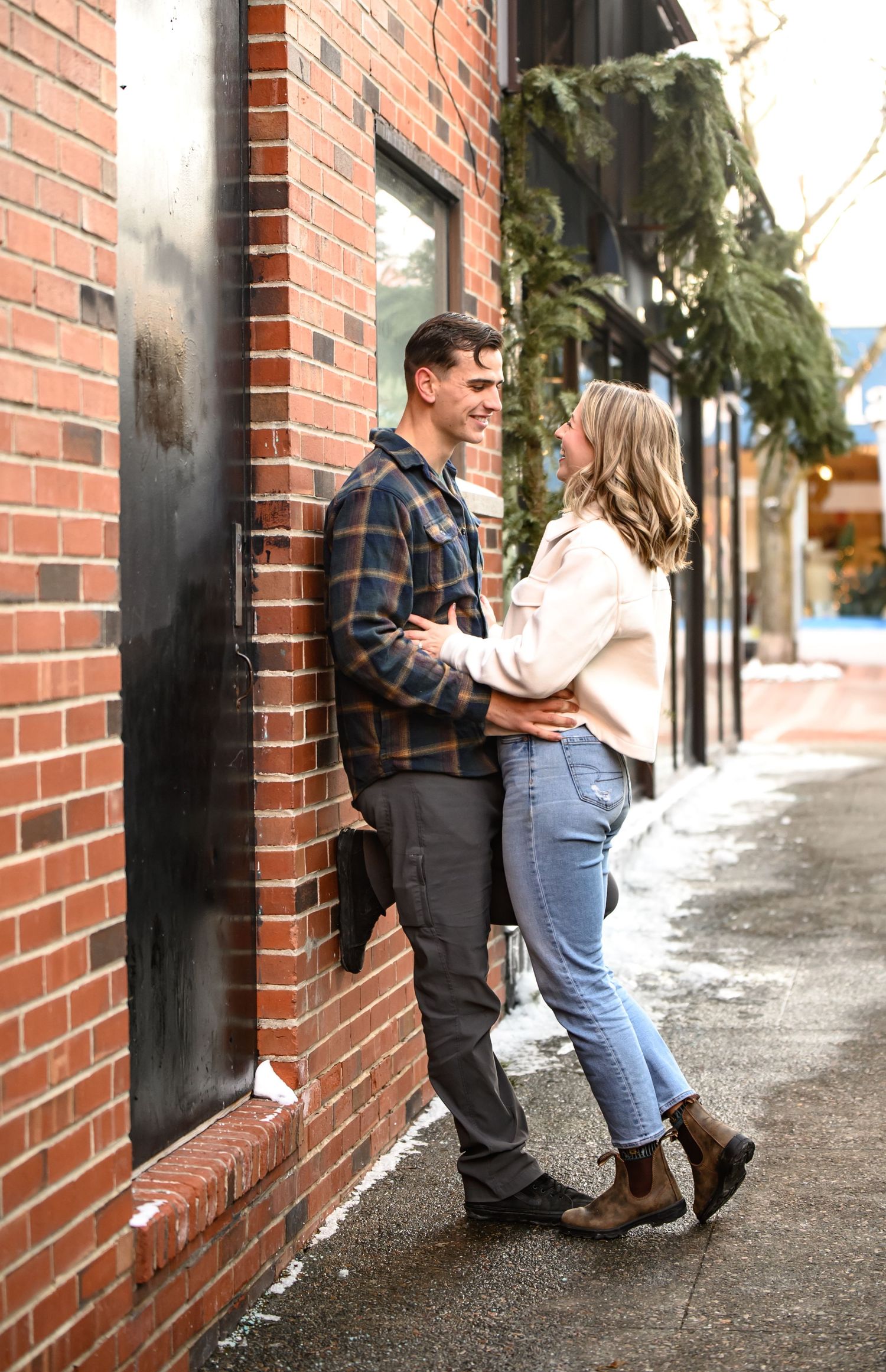 Couple in casual wear leaning against brick wall in series of romantic poses on urban sidewalk.