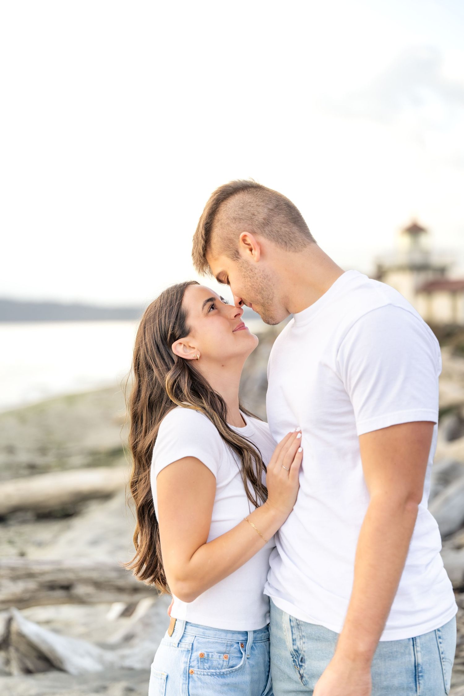 A romantic couple in matching white t-shirts and jeans share intimate moments on a beach at sunset.