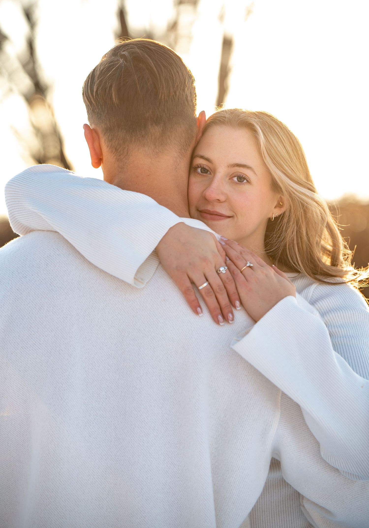 A couple shares an intimate moment at sunset with soft golden light illuminating their embrace.