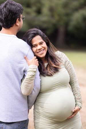 A joyful maternity photoshoot in a park shows a couple embracing and celebrating their pregnancy journey.