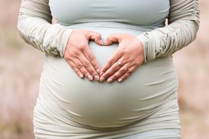 Close-up progression photos showing a growing baby bump during pregnancy in a beige dress.