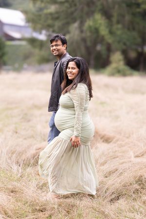 A couple shares tender moments while posing in a rustic field with dried grass and trees in the background.