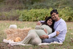 Couple lying on grass during outdoor maternity photoshoot in casual attire.