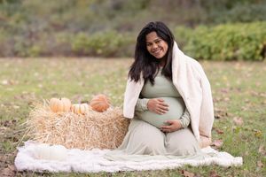 A maternity photoshoot in a rustic outdoor setting with hay bales and autumn decor.