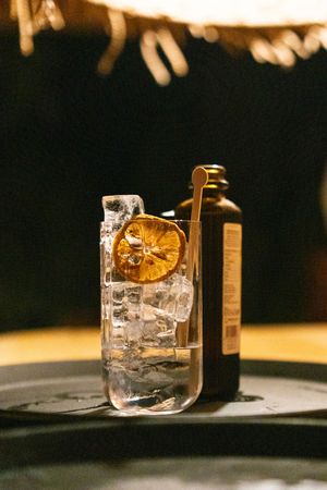 Crystal clear cocktail glass with large ice cube and garnish on dark surface.