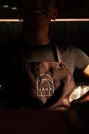 Dark leather apron with JAGA logo illuminated in moody lighting at a bar.