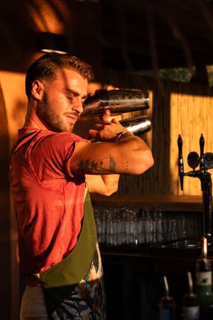 Bartender in red shirt demonstrating cocktail preparation techniques in dramatic lighting.