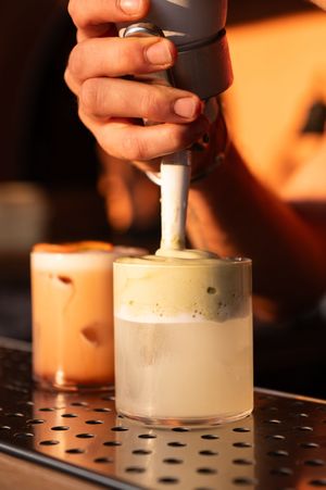Hands piping white cream onto a dark surface in warm lighting.