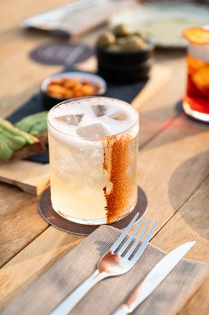 Artisanal cocktail with frost-dusted glass served on wooden table with dining utensils.