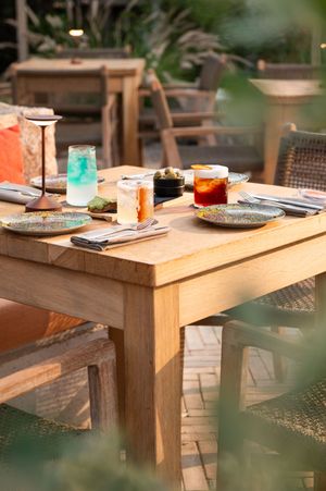 Wooden outdoor dining table set with colorful drinks and place settings in garden setting.