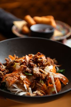 Close-up of a savory Asian noodle dish with meat and vegetables in a dark ceramic bowl.