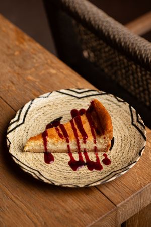 Artistic plating of a dessert with red sauce drizzle on a textured cream-colored plate.