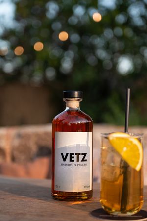 Bottle of Vetz spirits next to crafted cocktail with orange garnish on wooden surface.
