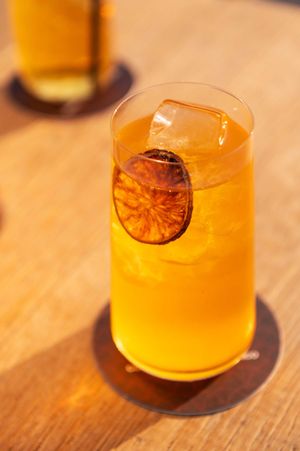 Orange-colored cocktail with dried citrus garnish on wooden table surface.
