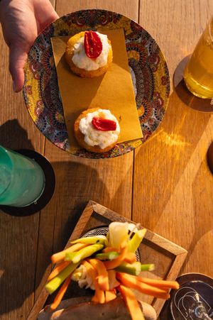 Appetizer plates and cocktails arranged on wooden table in sunlit setting.
