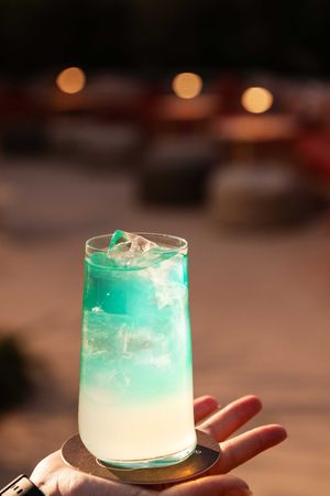 A vibrant turquoise cocktail with layered gradient effect served in a rocks glass.