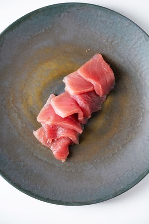 Slices of fresh raw tuna sashimi arranged on a rustic dark ceramic plate, perfect for Japanese cuisine.