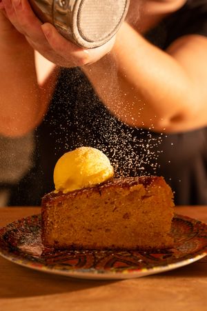 Powdered sugar being sprinkled over a slice of cake with yellow garnish.
