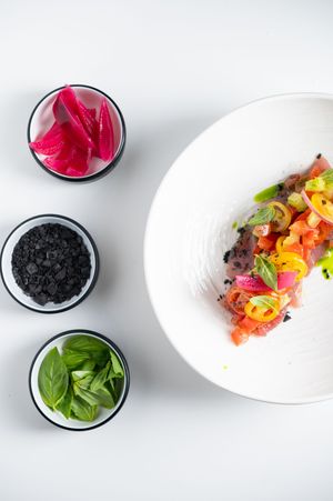 Elegant fine dining dish with colorful tuna tartare on white plate, served with pickled onions, black salt, and fresh basil.