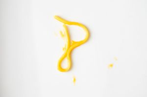 Yellow mustard squirted in the shape of the letter P on a white background.
