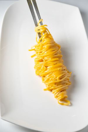A fork twirled with fresh yellow egg noodles served on a white ceramic plate.