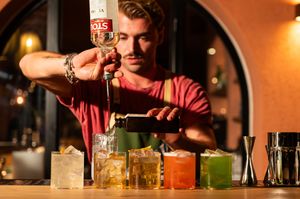 Bar counter with colorful cocktails being prepared in warm ambient lighting.