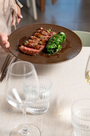 Sliced medium-rare steak served on a brown plate with sautéed greens, presented at a restaurant table.