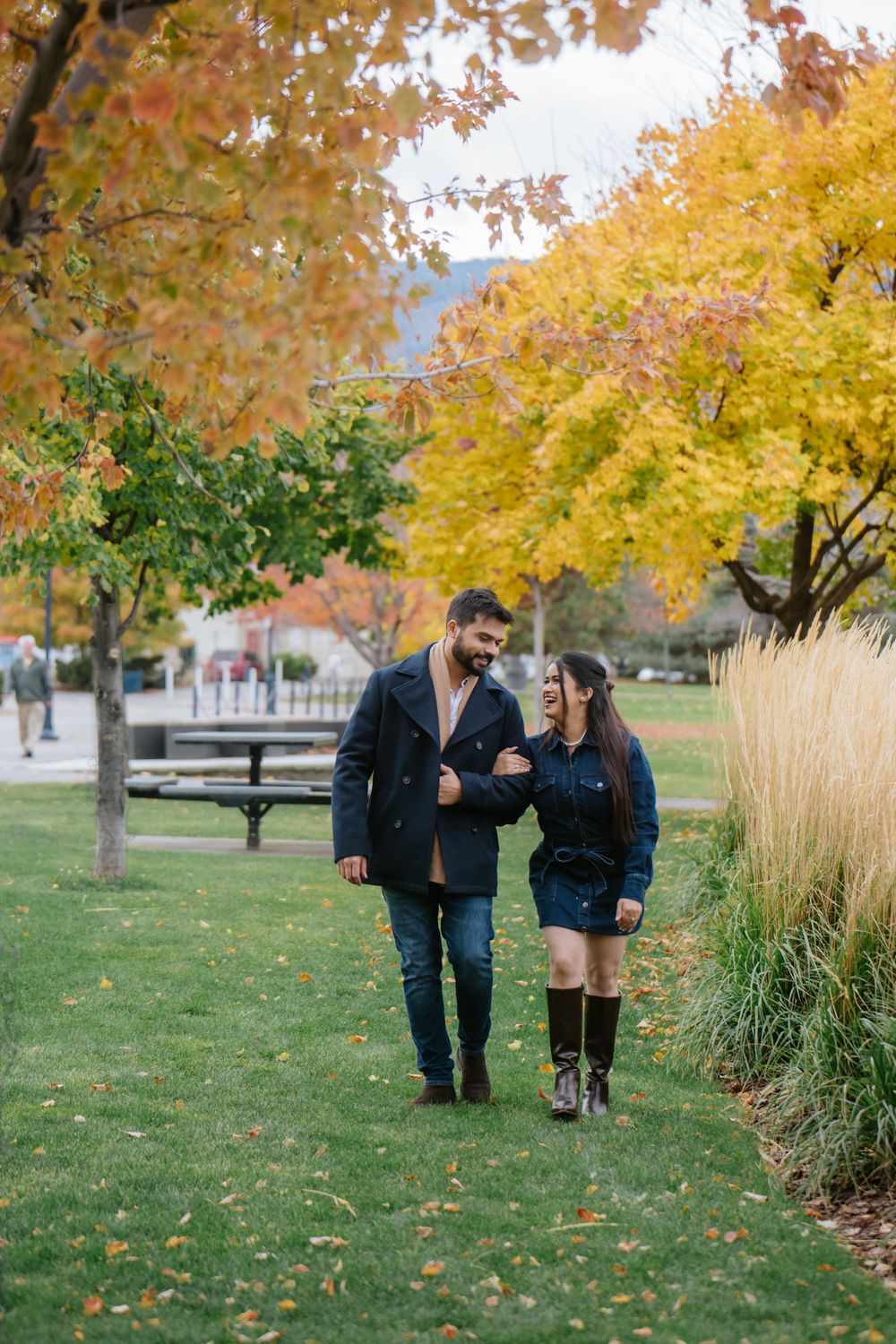 A couple strolls together on a path surrounded by vibrant fall foliage in a park setting.