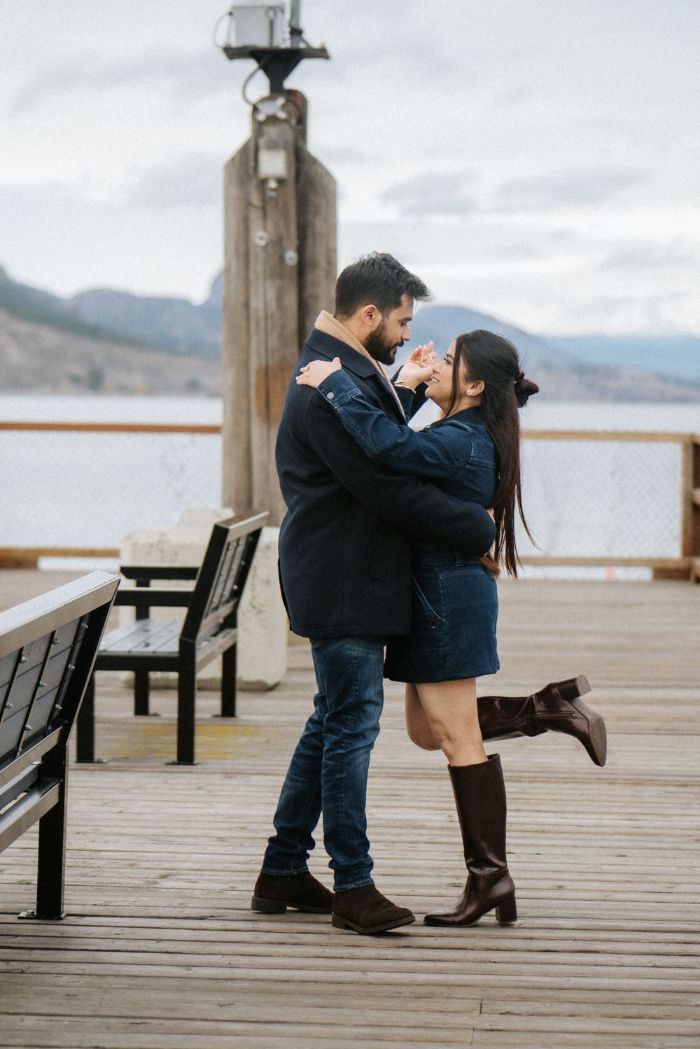 A romantic moment between a couple embracing on a wooden dock overlooking a misty mountain landscape.