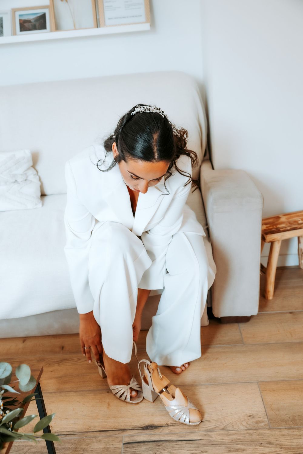 A person in a white robe adjusts their sandals on a light wooden floor.