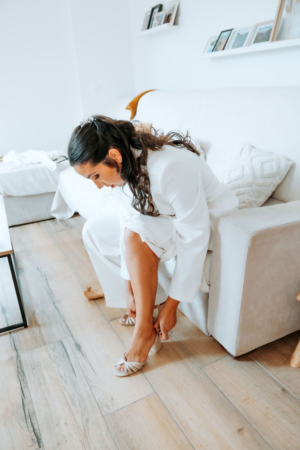 A person in white bends down on a light wooden floor in a minimalist room.