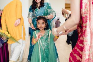Adorable young girl in teal Indian lehenga dancing at a colorful wedding celebration.