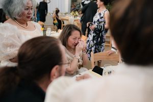 Emotional wedding guest wiping tears at reception table surrounded by family members.