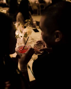 Couple clinking cocktail glasses at a warmly lit wedding reception dinner table.
