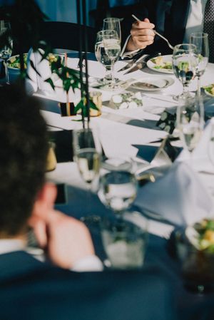 Elegant wedding reception table setting with champagne glasses and guests dining in bright sunlight.