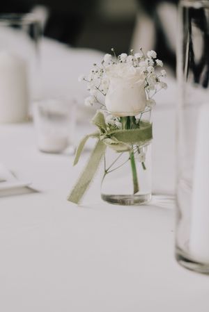 Minimalist wedding table centerpiece with white rose and baby's breath in a small glass vase.