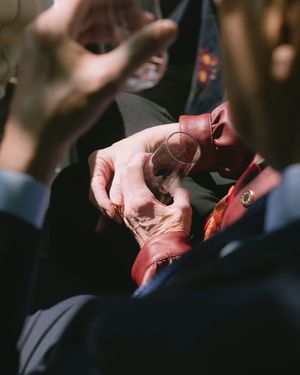 Close-up of elderly hands holding a wedding ring with a colorful floral boutonniere in soft sunlight.