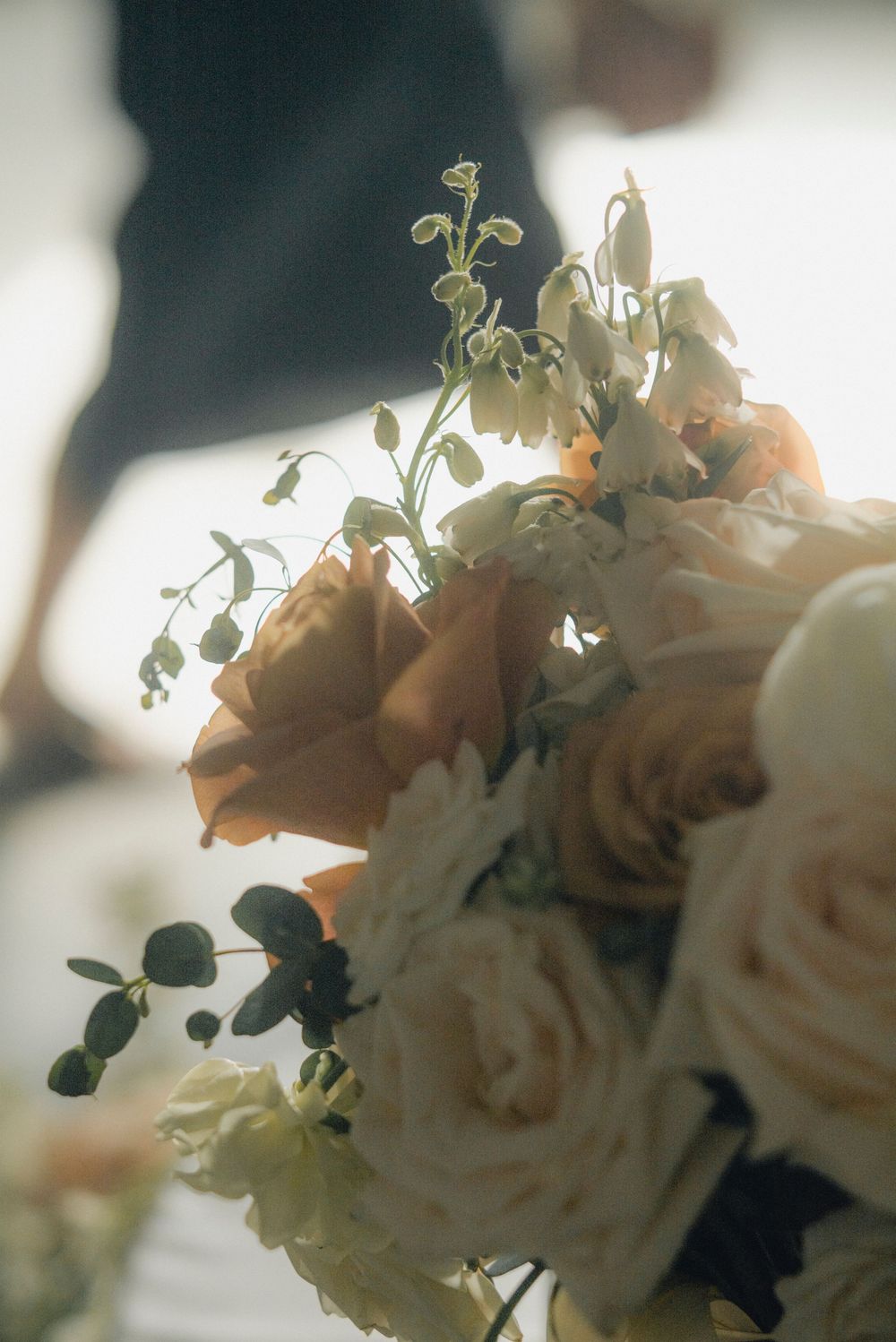 Close-up of a bridal bouquet featuring peach roses, white blooms, and delicate greenery in soft light.