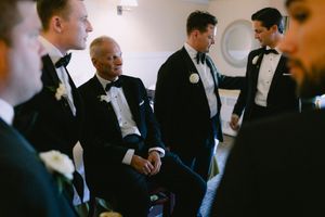 Groomsmen in black tuxedos with bow ties share a candid moment together before the wedding ceremony.