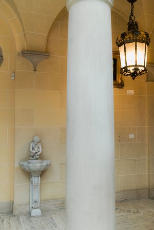 Elegant venue portico with a white marble column, ornate hanging lantern, and cherub fountain statue.