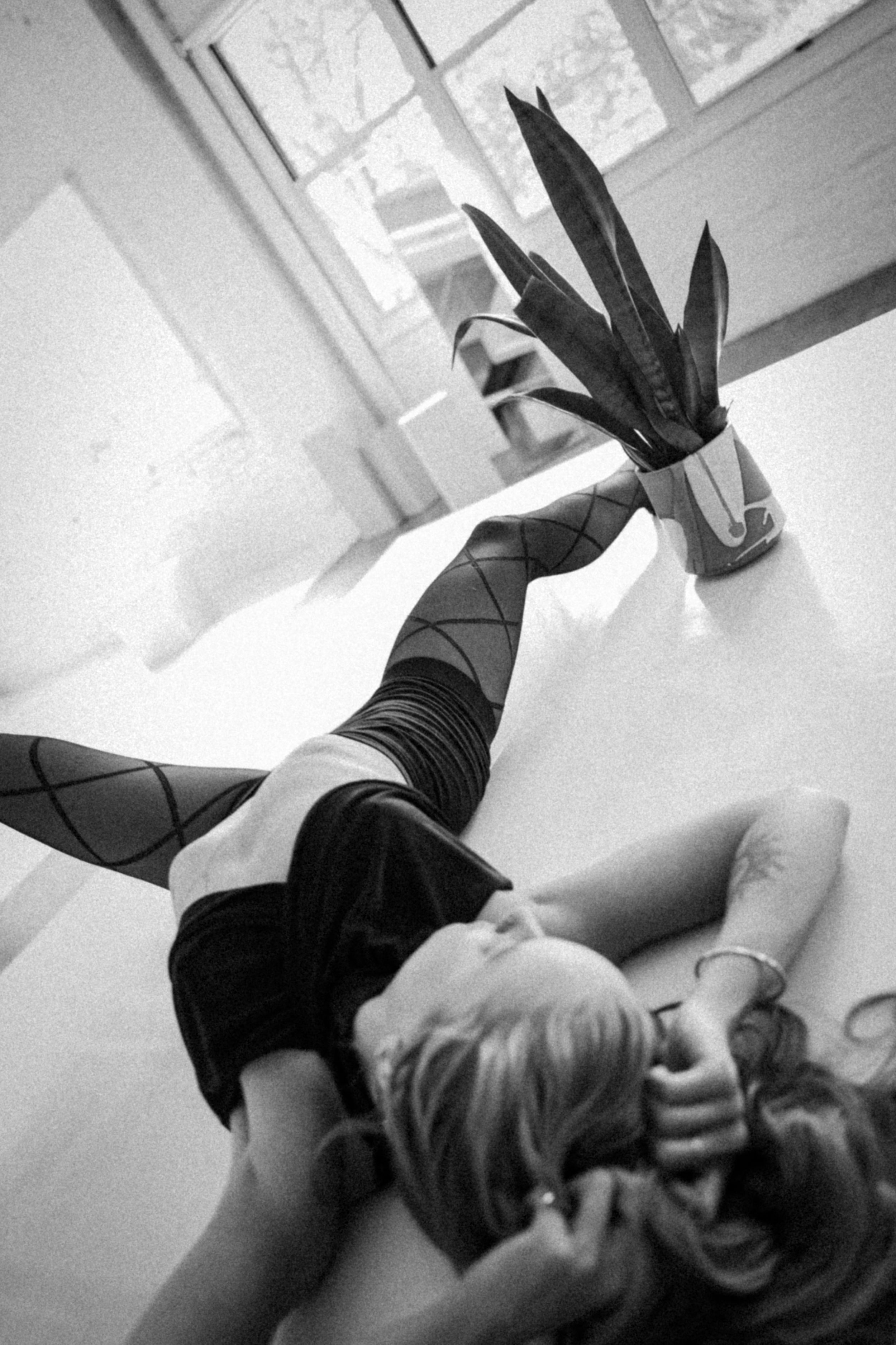 Artistic black and white photo of a person lounging with a potted plant near a window.