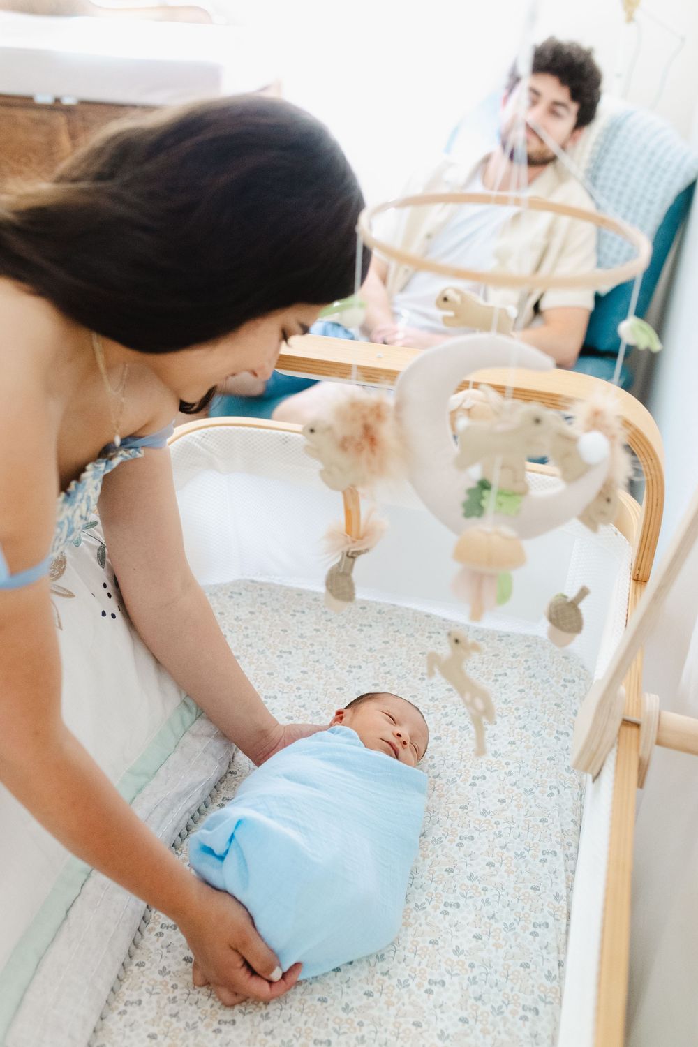 A tender moment in a nursery as a parent leans over a crib to check on their sleeping newborn baby.