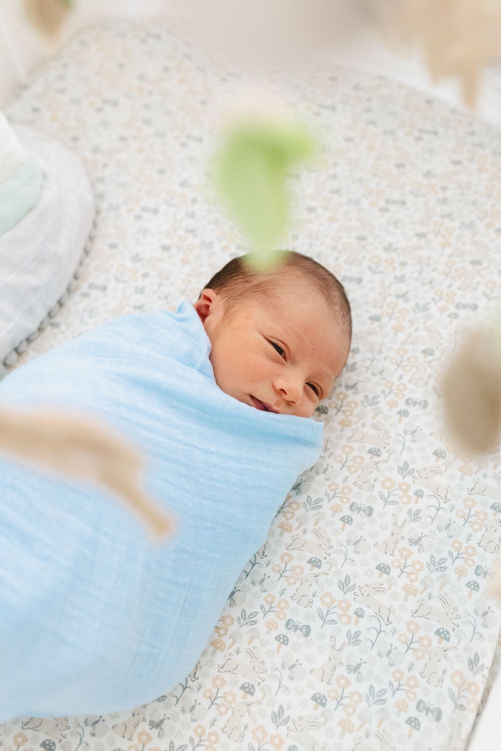 Sleeping newborn baby swaddled in blue blanket on floral patterned bedding.