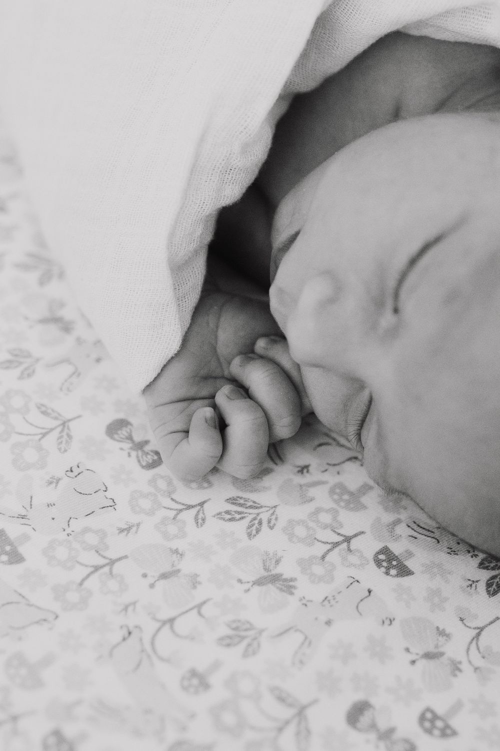 Close-up black and white photo of tiny baby fingers grasping against a floral patterned blanket.