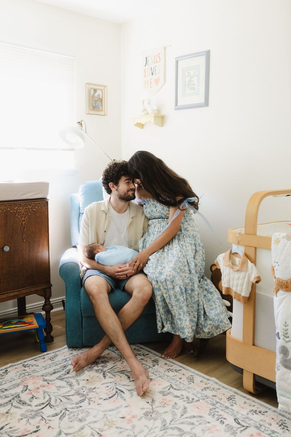 A couple shares an intimate moment in a cozy nursery decorated with floral rugs and framed artwork.