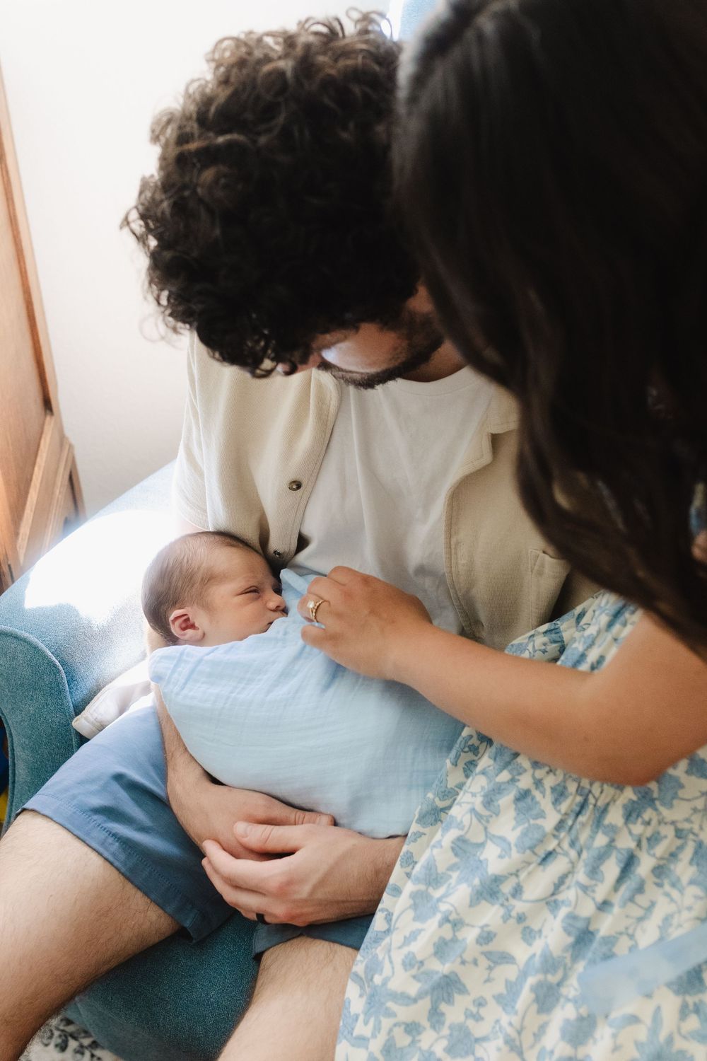 Parents tenderly care for their newborn baby dressed in light blue in a bright nursery setting.